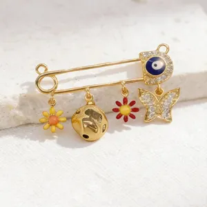 Gold safety pin charm pendant detail with evil eye, flowers, and crystal butterfly accents.
