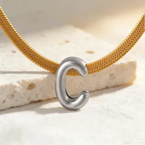 Nahaufnahme einer goldenen Schlangenkette mit silbernen dicken Buchstaben C Anhänger.