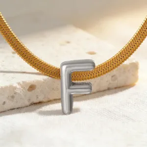 Nahaufnahme Detail eines silbernen Buchstaben F Anhängers an goldener Schlangenkette.