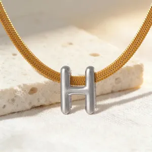 Detailaufnahme des silbernen Buchstaben-H-Anhängers an einer goldenen flachen Schlangenkette.