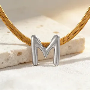 Nahaufnahme Detail der goldenen Schlangenkette mit elegantem silbernem Buchstabe M Anhänger.