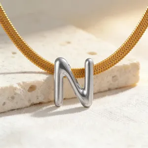 Nahaufnahme Detail des silbernen gepufften Buchstaben N Anhängers an goldener flacher Schlangenkette.