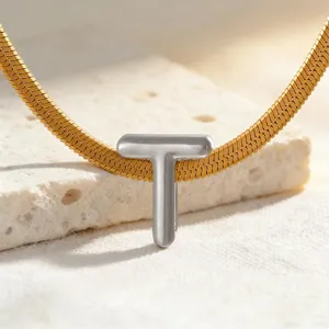 Detailaufnahme des eleganten silbernen Buchstaben-T-Anhängers an der goldenen Schlangenkette.