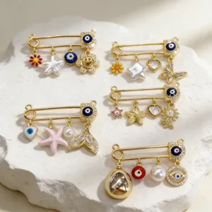 Close-up of gold-tone evil eye safety pin charms with pearls, starfish, and crystal details.