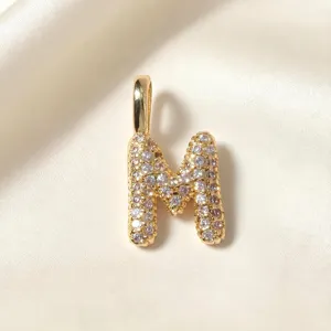 Gouden letter M hanger detail, sprankelende zirkoniastenen op glanzend gepolijst metaaloppervlak.
