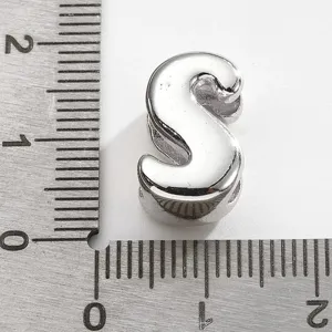 Gros plan détaillé d'un charm lettre S en argent présenté avec une règle de mesure.