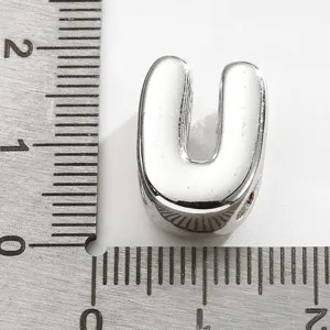 Gros plan d'un pendentif en métal lettre U argentée à côté d'une règle montrant sa taille réelle.