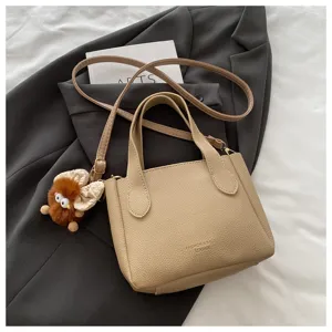 Vista detallada del bolso beige de cuero sintético con textura graneada y lindo dije.
