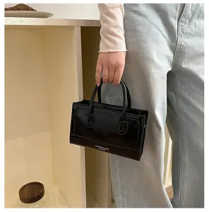Detail shot of black structured handbag, compact minimalist design with double top handles.