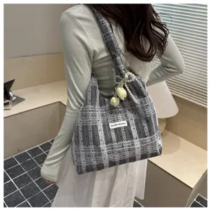 Detailed shot of a stylish grey plaid canvas tote bag with pearl tulip pendant worn by model.