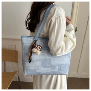 Λεπτομερής εικόνα της κομψής μπλε τσάντας tote patchwork με χαριτωμένο λούτρινο αξεσουάρ.