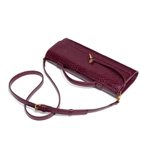 Close-up detail of burgundy crocodile pattern faux leather baguette bag with gold hardware.