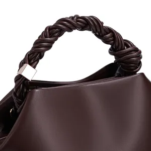 Close-up detail of stylish brown women handbag featuring elegant braided handle and metal accent.