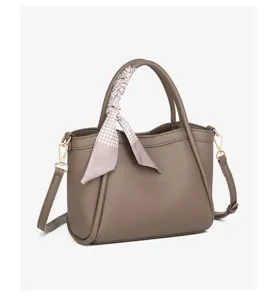 Vista detallada del bolso tipo cubo de cuero marrón con pañuelo elegante y herrajes dorados.
