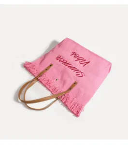 Bolso de playa tejido rosa con asas de cuero marrón, flecos y detalles de bordado de verano.