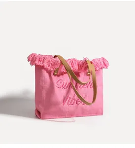 Bolso tote de lona rosa con flecos superiores y diseño de letras bordadas para playa y uso diario.