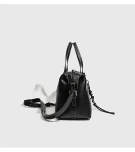 Bolso boston de piel negra vista lateral con textura lisa, costuras blancas y correa.