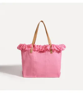 Detalle de bolso tote rosa con flecos, tejido texturizado, asas marrones y remaches.