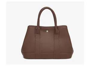 Brown leather tote bag detail showing textured finish, dual handles and center snap button.