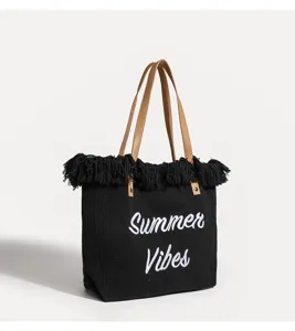 Bolso tote de lona negra con flecos superiores, asas marrones y bordado blanco de verano.