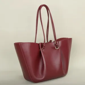 Burgundy leather tote bag detail showing pleated sides and dual straps with metal rings.