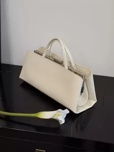 Detailansicht einer minimalistischen cremeweißen Handtasche mit Metallrahmen und Henkeln.