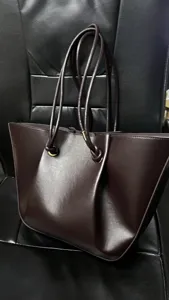 Brown leather tote bag close-up showing pleated design, thin shoulder straps and metal rings.