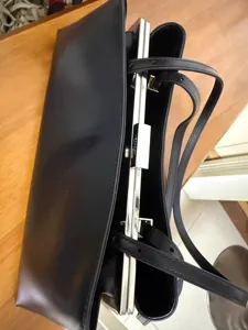 Detailansicht einer schwarzen Lederschultertasche mit Metallrahmen-Verschluss und schmalen Riemen.