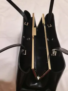 Detailansicht einer eleganten schwarzen Lederhandtasche mit Goldmetallrahmen und Innenseite.