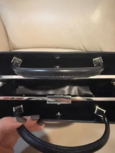 Detailaufnahme einer schwarzen Ledertasche mit Metallrahmenverschluss und doppelten Griffen.