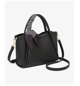 Primer plano del bolso de cuero negro con un elegante pañuelo de pata de gallo en el asa.