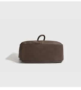 Detailopname van de bruine lederen handtas, met fijne textuur en een minimalistische handgreep.
