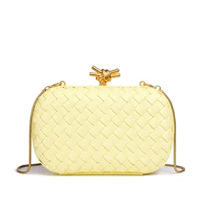 Gelbe gewebte Box-Clutch Tasche Detail mit goldenem Metall-Knotenverschluss Kette.