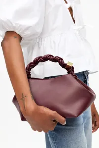 Burgundy leather handbag featuring a stylish braided handle and gold metal hardware accent.