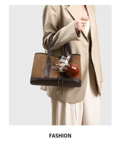 Detailopname van de stijlvolle tweed tas met chique lederen afwerking en berenhanger.
