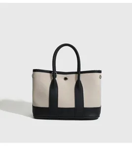 Primo piano della borsa tote in tela con finiture in pelle nera e dettaglio di chiusura.