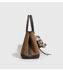 Gedetailleerd overzicht van de bruine tweed visgraat tas met lederen afwerking en berenhanger.