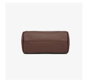 Detalle de bolso cilíndrico de piel marrón, material texturizado, diseño minimalista.