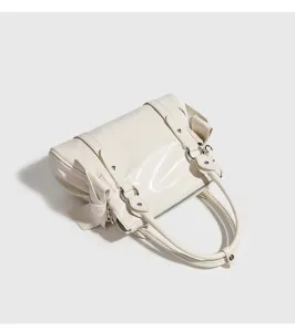 Detailed view of a cream white patent leather handbag featuring cute side bows and durable dual handles.