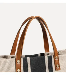 Nahaufnahme der braunen Ledergriffe und Nieten an der robusten Canvas-Stofftasche.