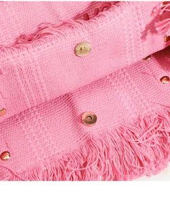 Primer plano detalle del bolso tote de tela tejida rosa con borde de flecos y botones dorados.