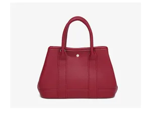Detailed view of red leather tote bag showing textured grain and sturdy dual handles.