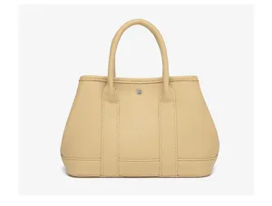Detailed view of the beige leather tote handbag featuring double handles and a central snap closure.