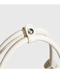 Close-up detail of white leather handbag handle with metal snap button and fine stitching.