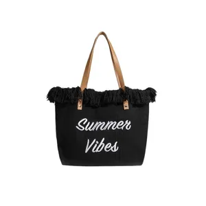 Bolso tote de lona negro con flecos asas marrones y texto bordado de verano chic.