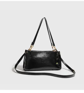 Bolso de hombro negro de cuero brillante con herrajes metálicos, correa y etiqueta elegante.