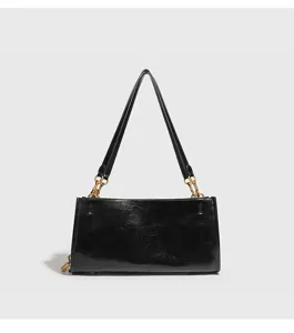 Detalle de bolso de hombro negro de piel sintética, cadena dorada elegante y cierre decorativo.