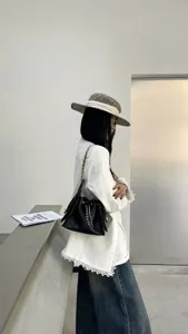 Detailed shot of black quilted leather chain bucket shoulder bag with elegant white outfit.