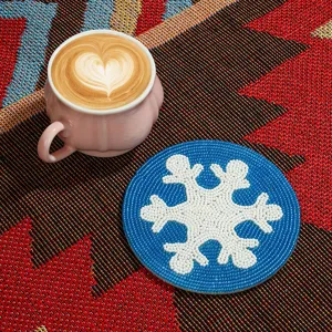 Gros plan d'un sous-verre rond en perles bleues fait main avec motif de flocon blanc.