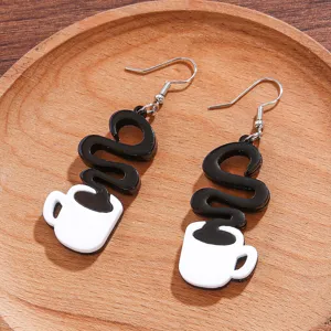Close-up detail of creative black and white coffee cup acrylic dangle earrings on wooden tray.